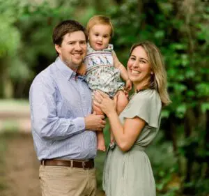 A happy family with a father, mother, and baby outdoors.